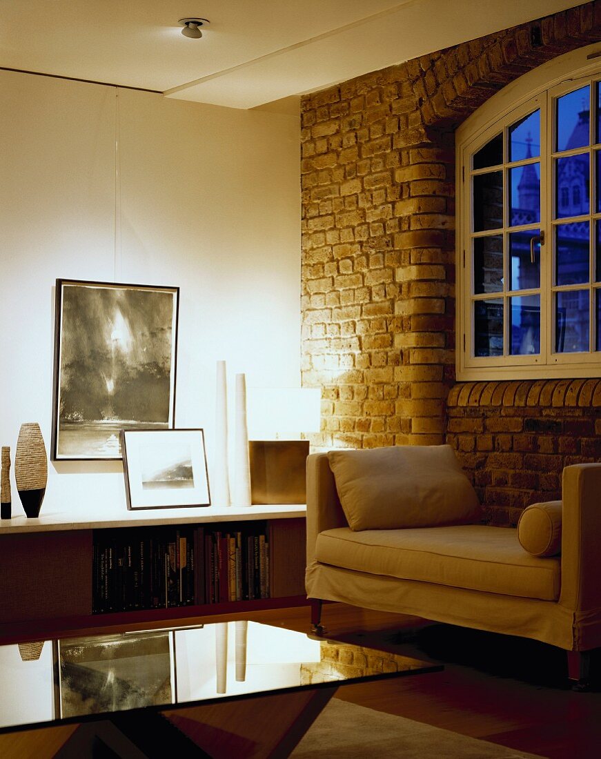 An elegant living room with a glass table and an upholstered couch against a brick wall