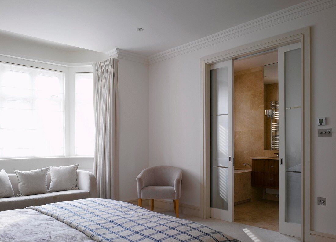 A white-painted bedroom with an en suite bathroom and a comfortable sofa