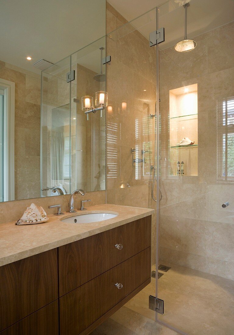 A bathroom with marble tiles and a glass partition wall separating the shower area
