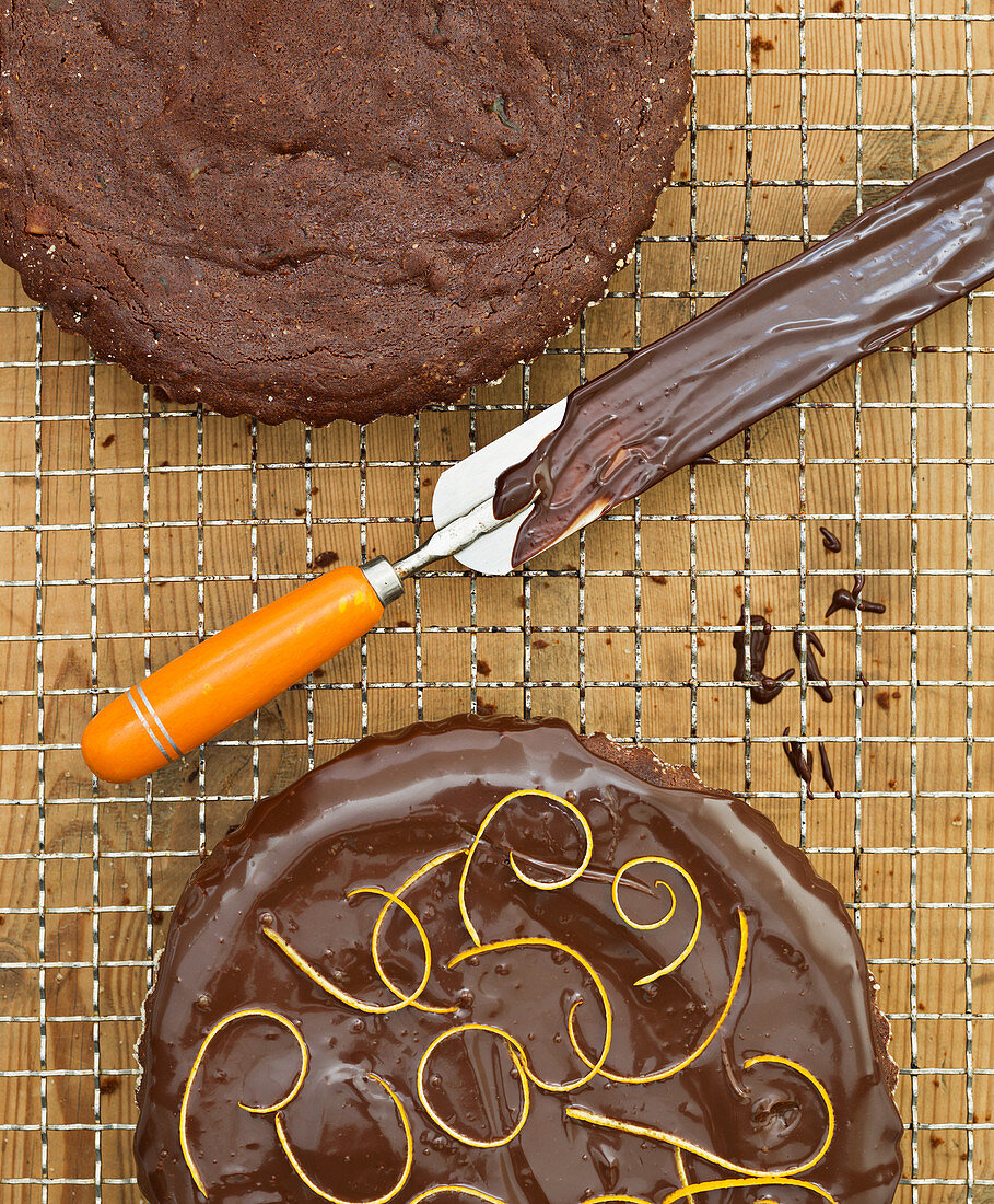 A chocolate cake on a wire rack being glazed