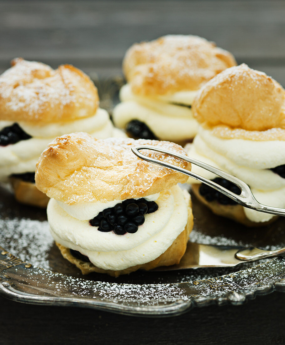 Profiteroles filled with cream and fresh blackberries on a silver plate
