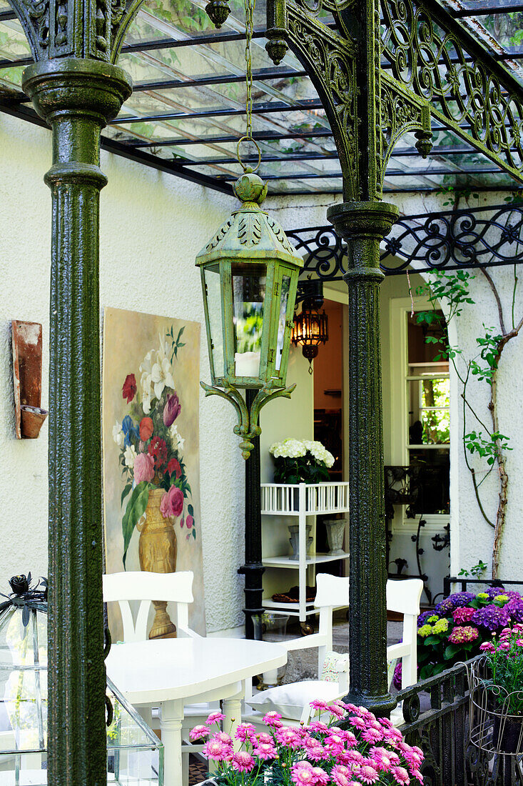 Terrasse mit Blumen, weißen Möbeln, antiker Laterne und Blumenbild