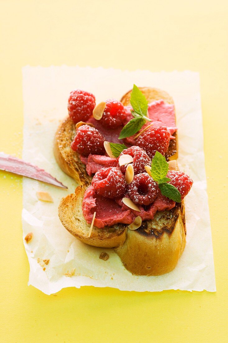 A sliced of toasted bread topped with raspberry butter and raspberries