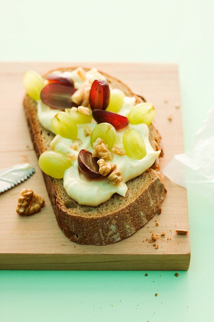 A slice of bread topped with cream cheese butter, grapes and nuts