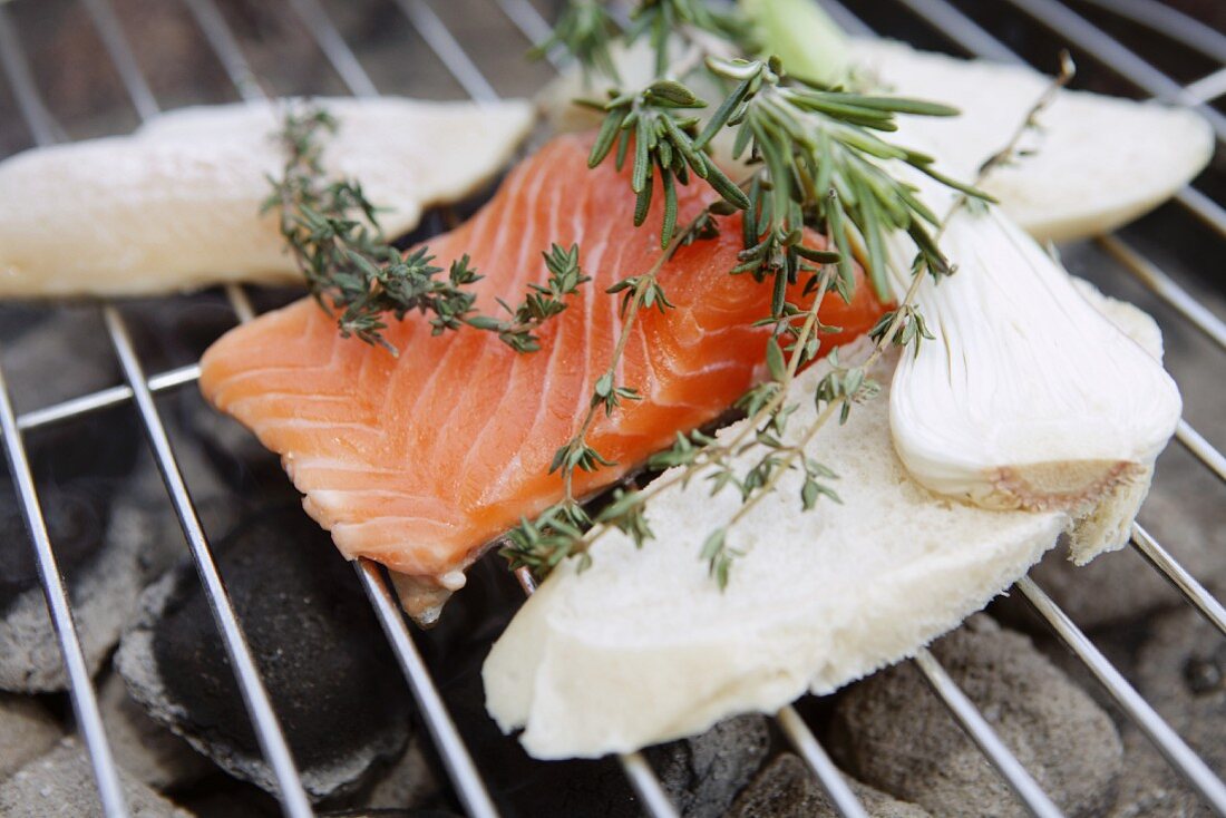 Lachsfilet und Brotscheiben auf einem Holzkohlegrill mit Kräutersträusschen