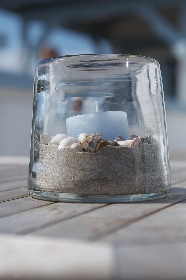 Light blue candle on bed of sand and shells in transparent candle lantern