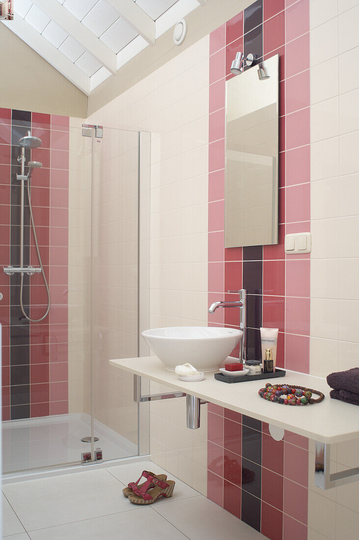 Bathroom with glass shower cubicle and washbasin, tiles in shades of pink, purple and white