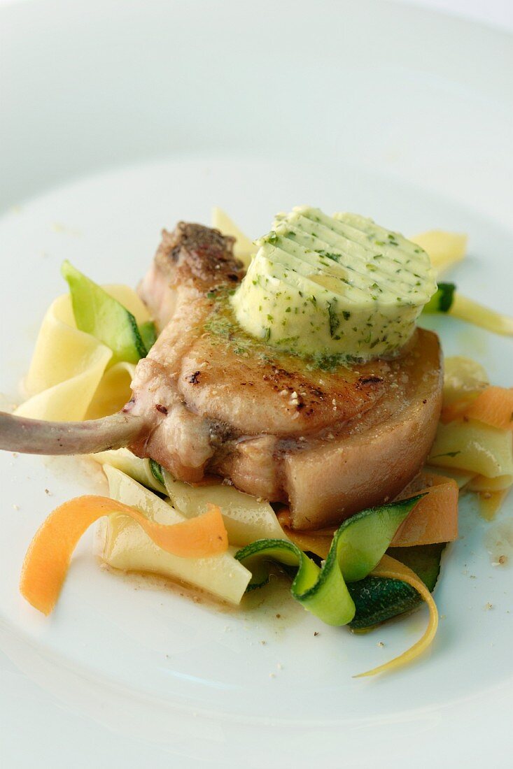 A pork chop with herb butter, vegetables and tagliatelle
