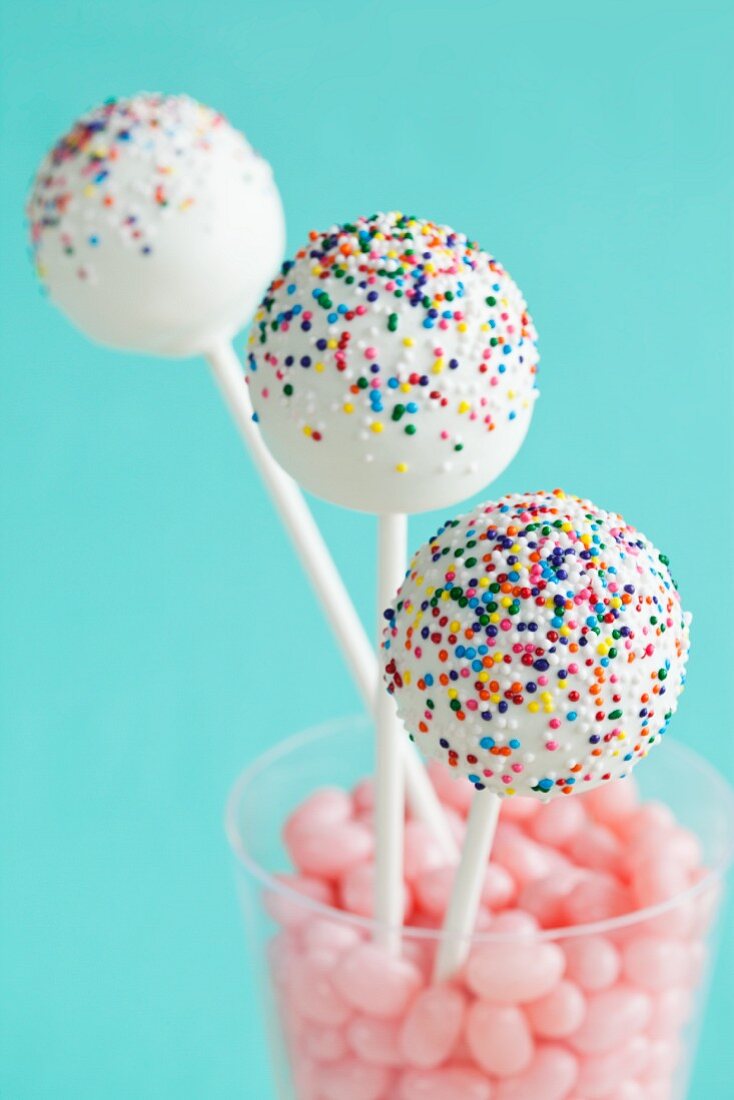 weiße Cake Pops mit bunten Zuckerperlen in einem Glas mit rosa Süssigkeiten