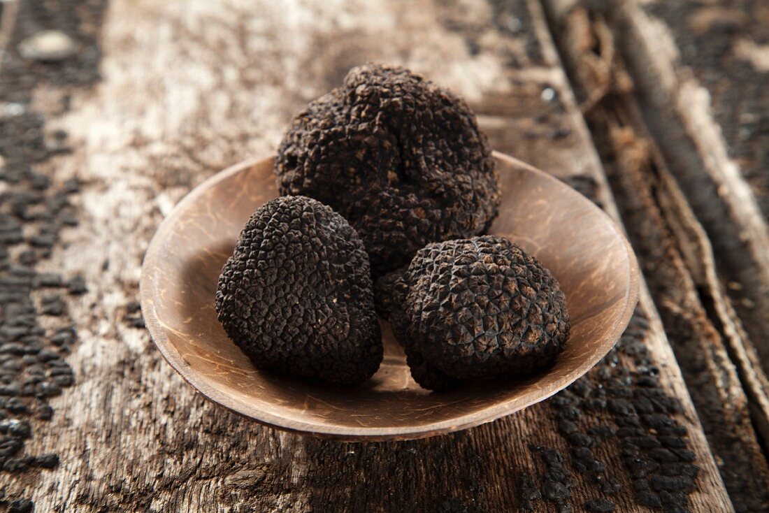 Three black truffles in a wooden bowl on a wooden surface