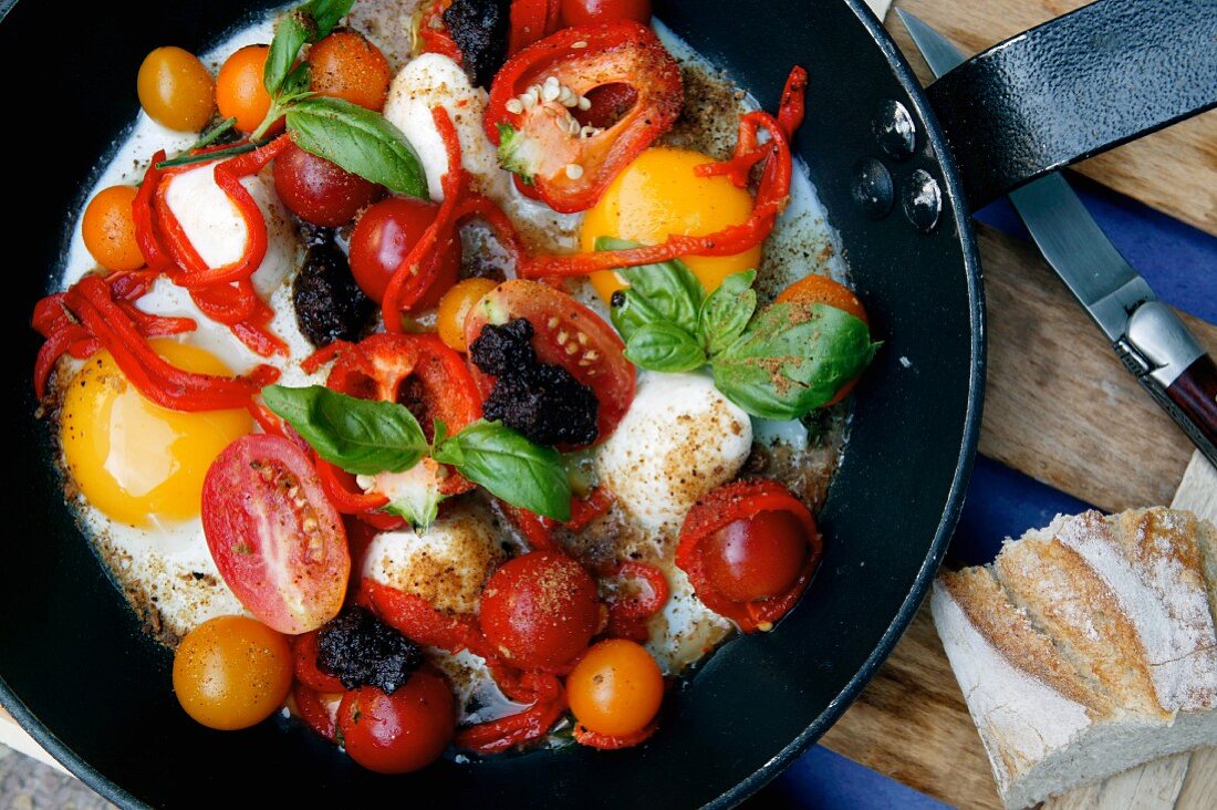 Fried eggs with tomatoes, olives and basil in a pan