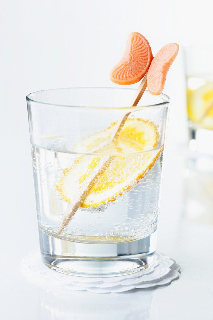 An orange slice and a stick in a glass of water