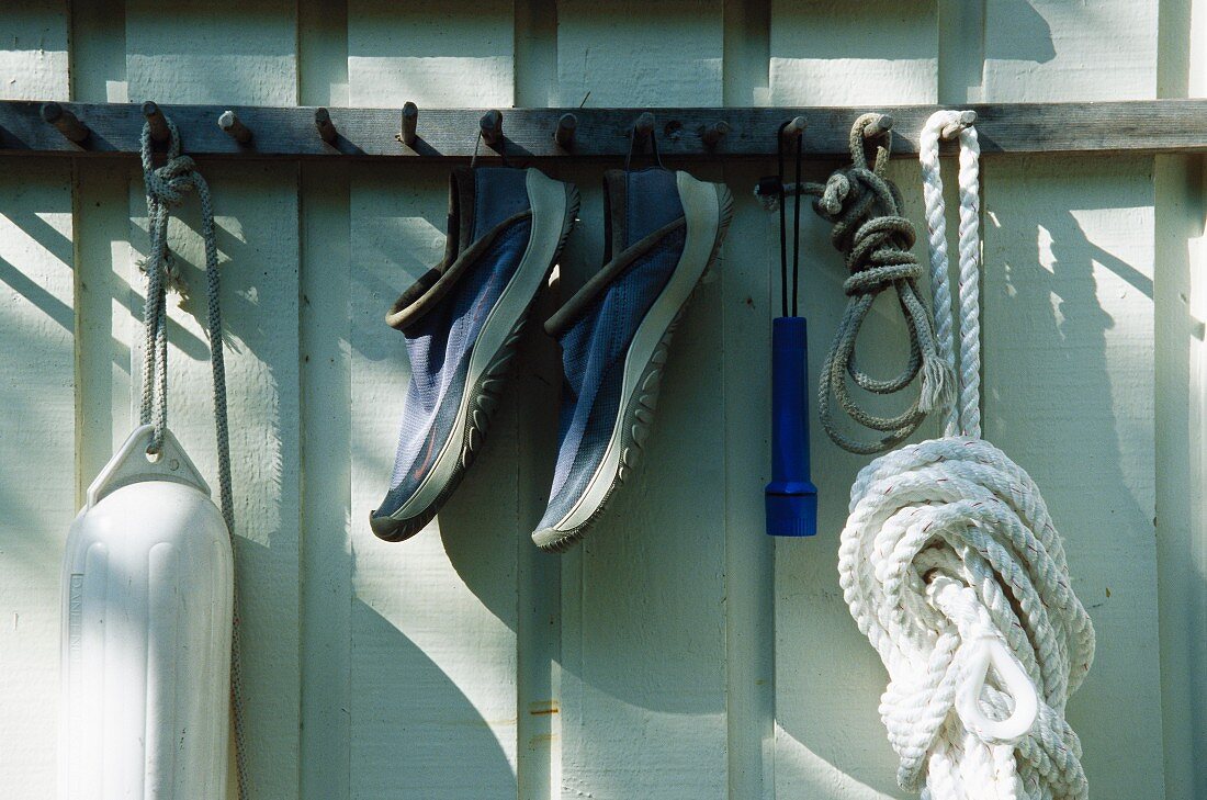 Buoy, pair of shoes and rope hanging from hooks on exterior wall of house