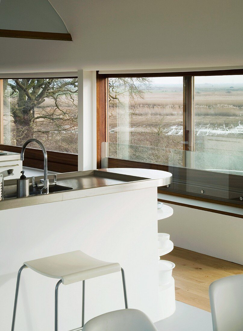 Kitchen island with stainless steel work surface in front of large windows in modern house