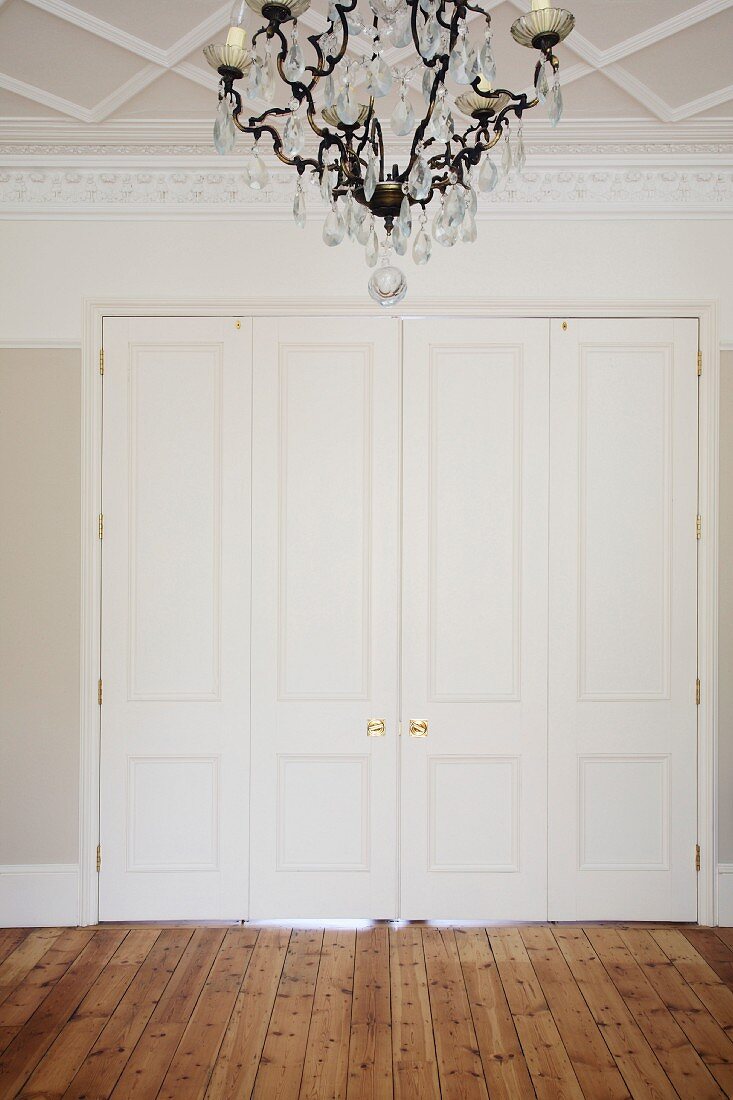 Wide hallway with chandelier, white double doors and wooden floor