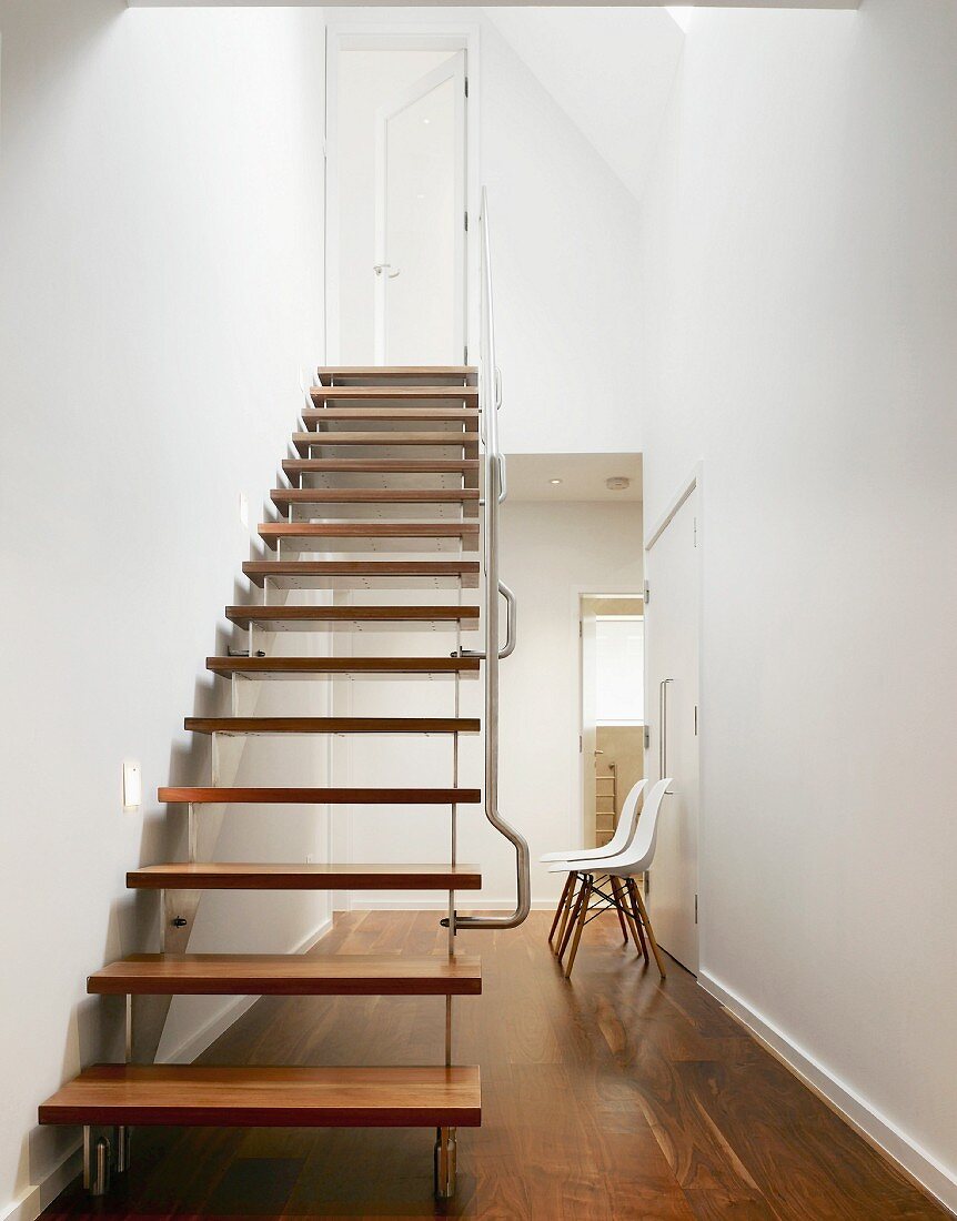 Designer staircase with wooden treads and stainless steel handrail in minimalist, open-plan stairwell