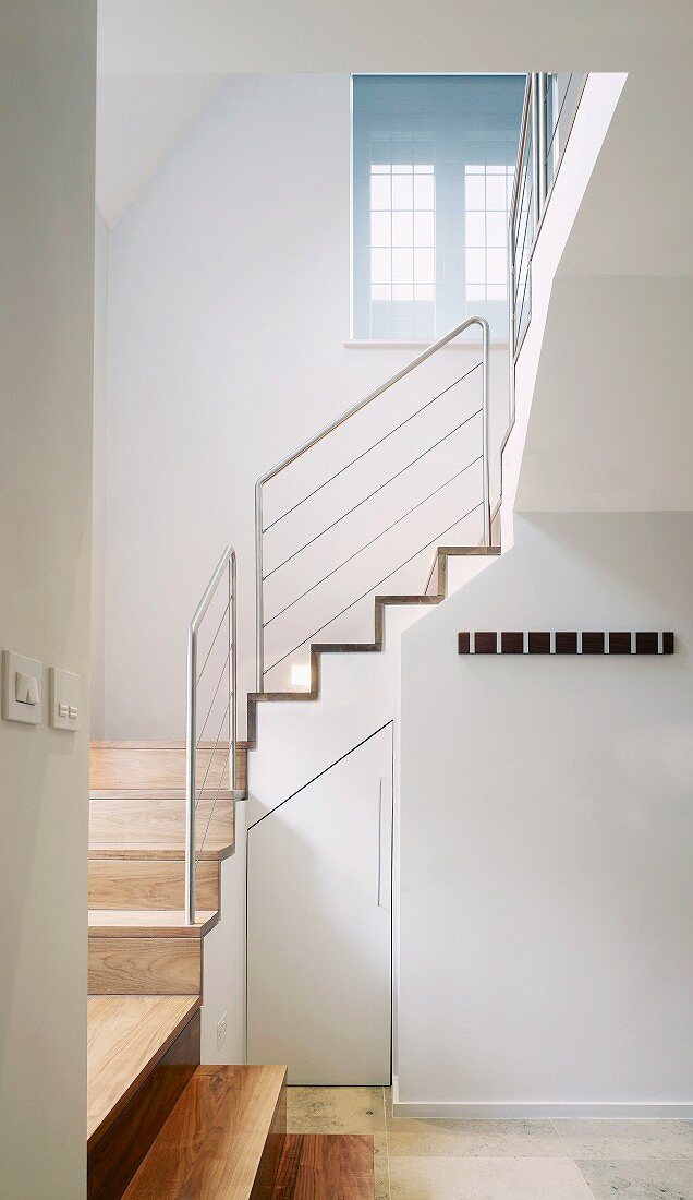 Weiß getöntes Treppenhaus mit Treppe aus Holz und Geländer aus Edelstahl