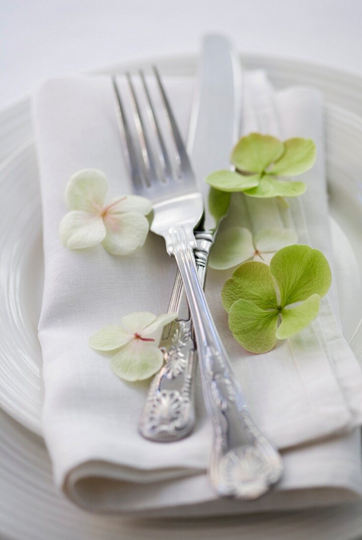 Place setting with silver cutlery on linen napkin and hydrangea florets