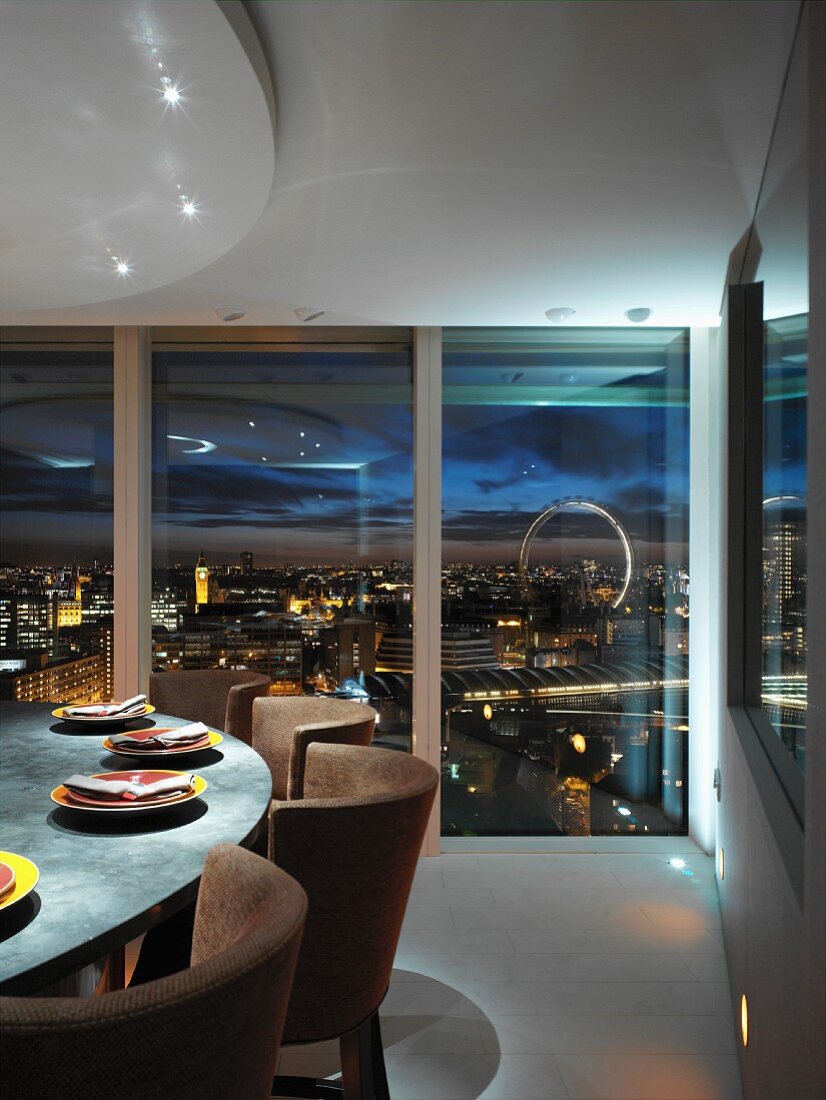 Set dining table in front of floor-to-ceiling glass wall and view of city lights