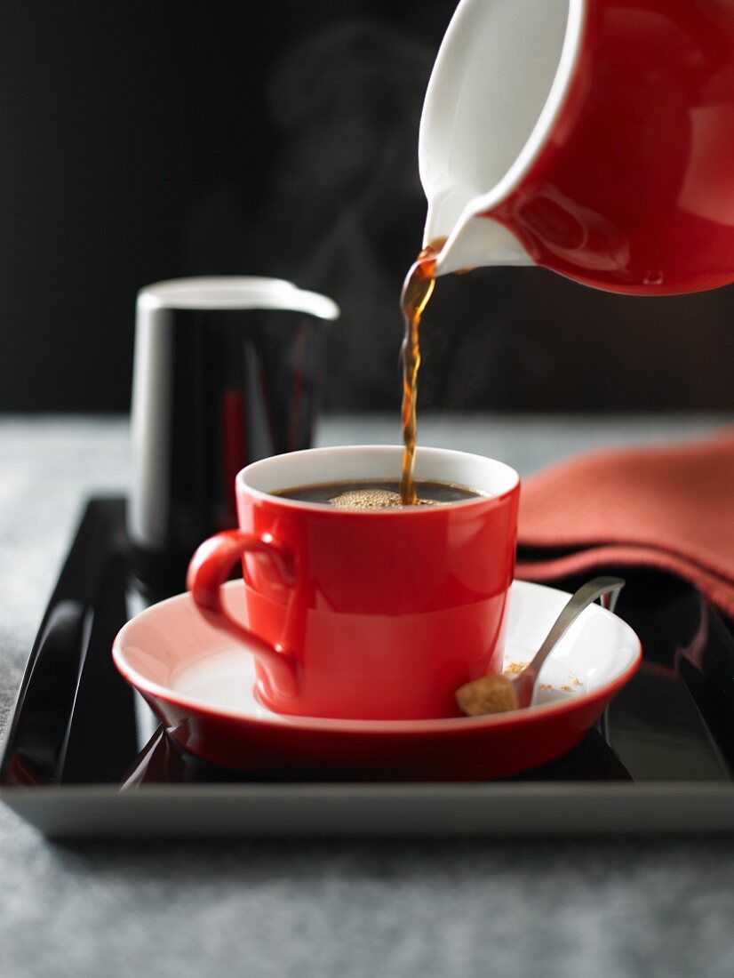 Hot Coffee Pouring From a Red Coffee Pot into a Red Coffee Cup