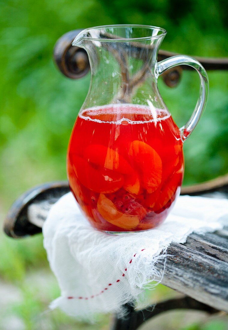 Punch with summer fruits in a pitcher on a garden chair