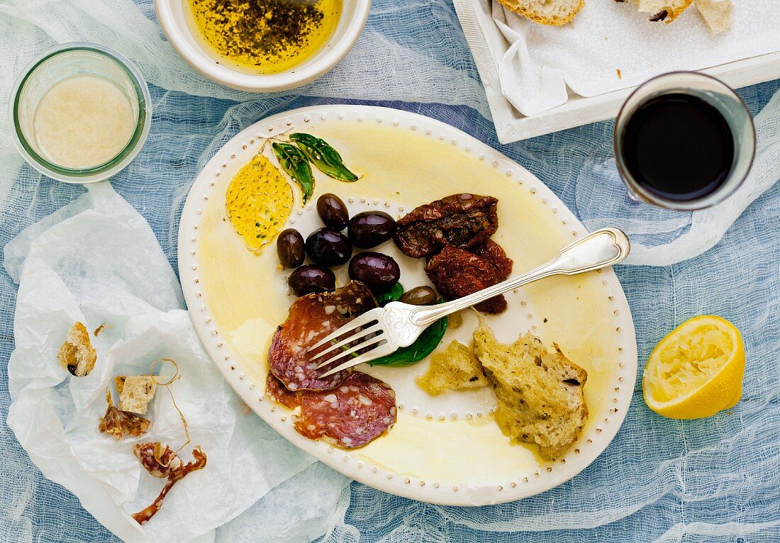 Antipasti-Teller mit Resten von Oliven, getrockneten Tomaten, Weißbrot und Salami