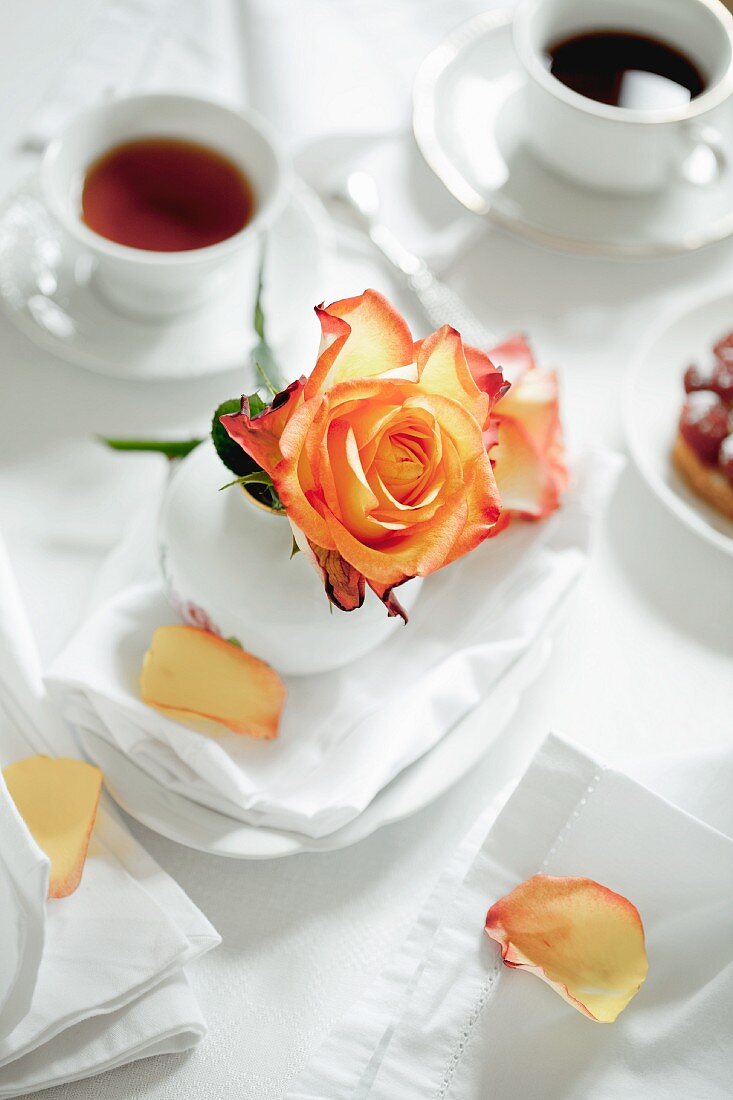 Eine Rose, Tee und Kaffee auf einem weiss gedeckten Frühstückstisch