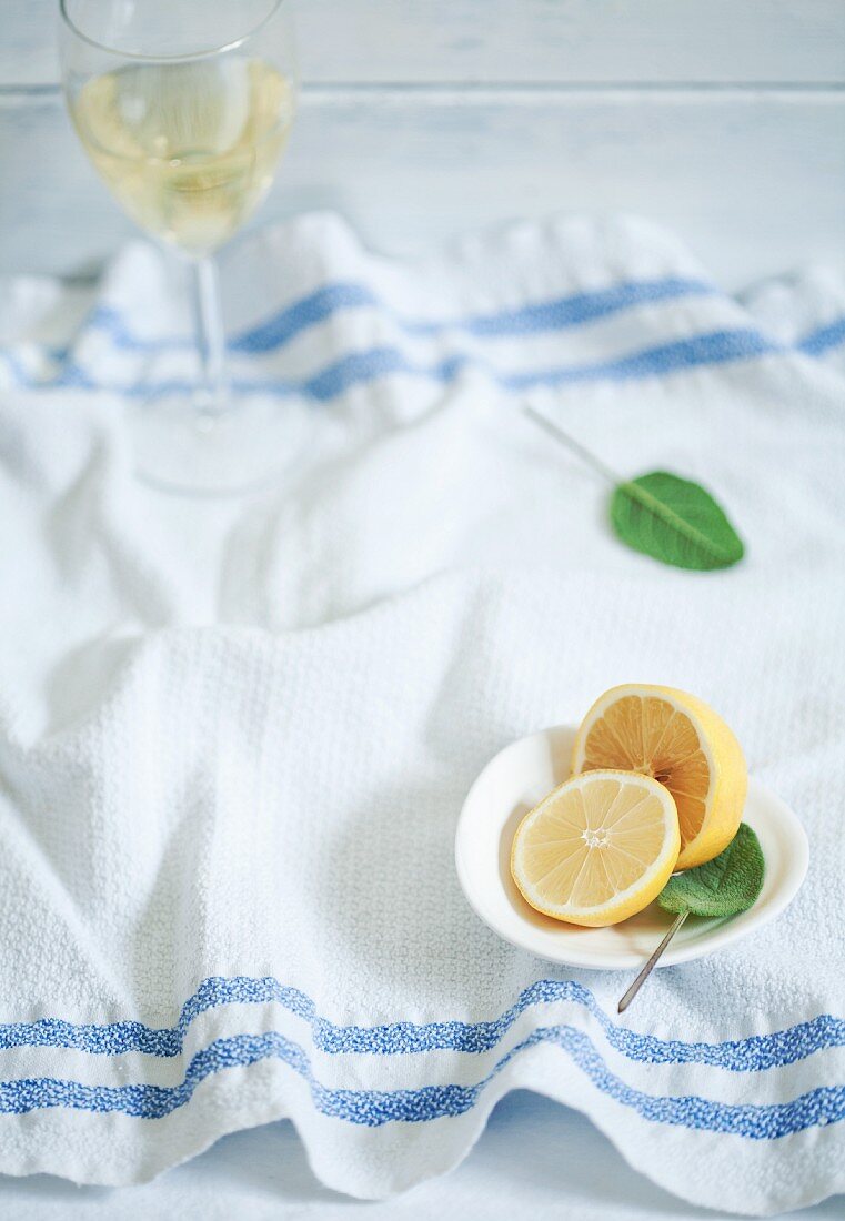 Fresh lemon, sage and a glass of white wine on a kitchen towel