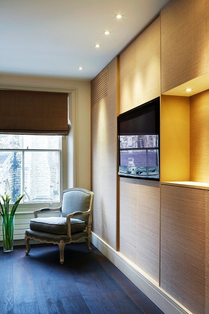 Bedroom wardrobe with integrated screen and antique armchair in front of window with fabric blind