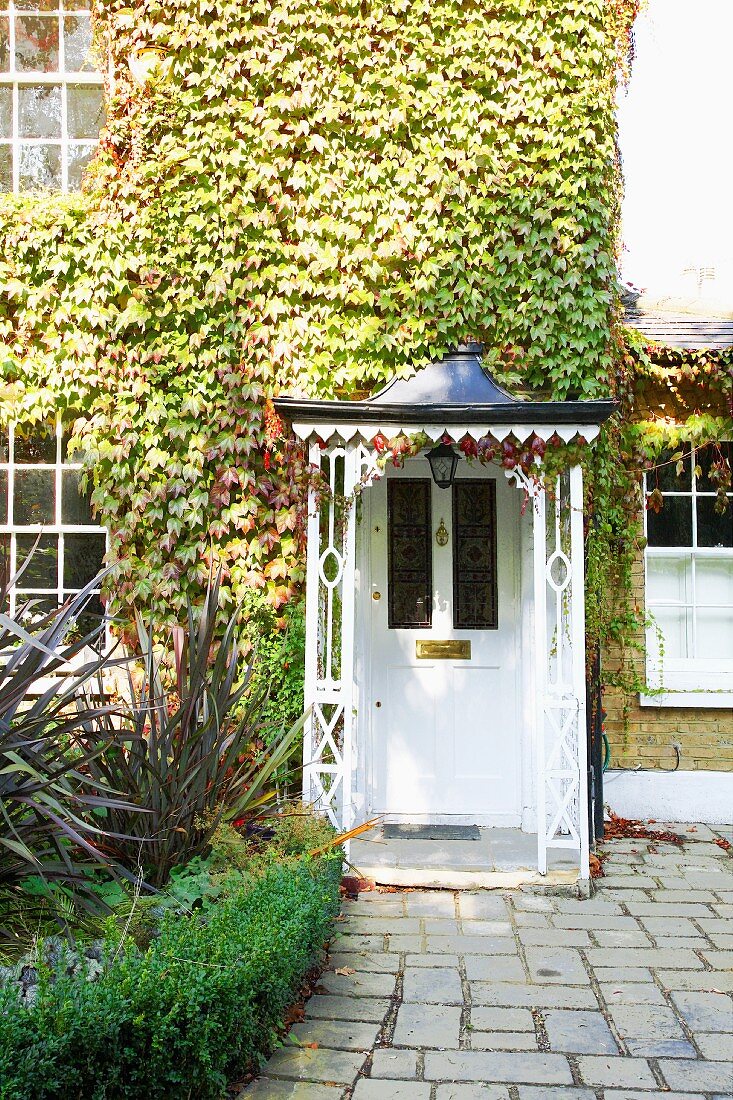 Historic, white front door with decorative copper porch below vine-covered facade