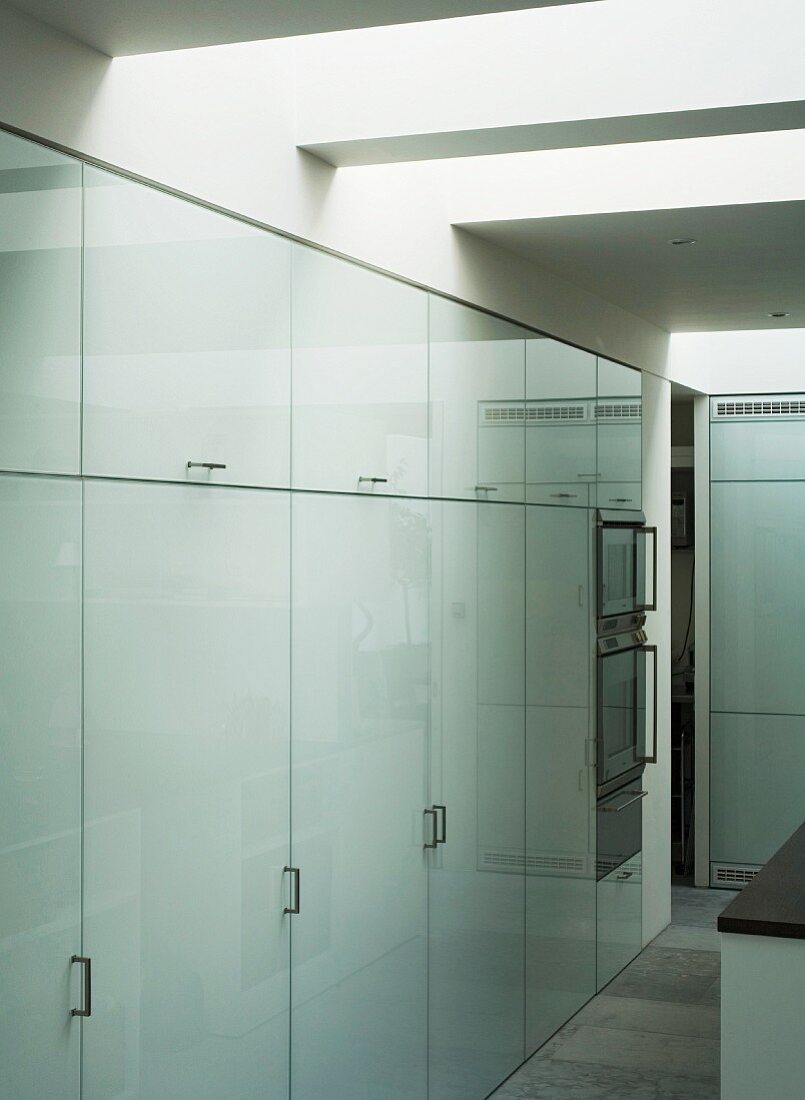 Wall of large, fitted cupboards with white glass doors and bracket handles