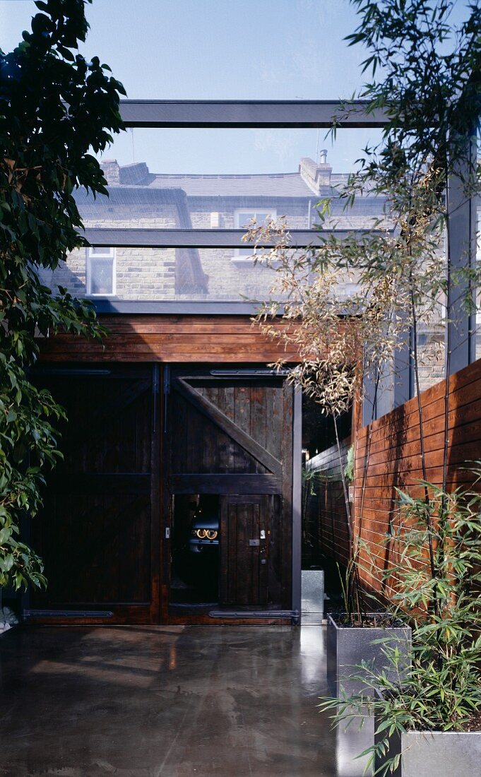 A partially covered courtyard with a barn door and bamboo in plant pots