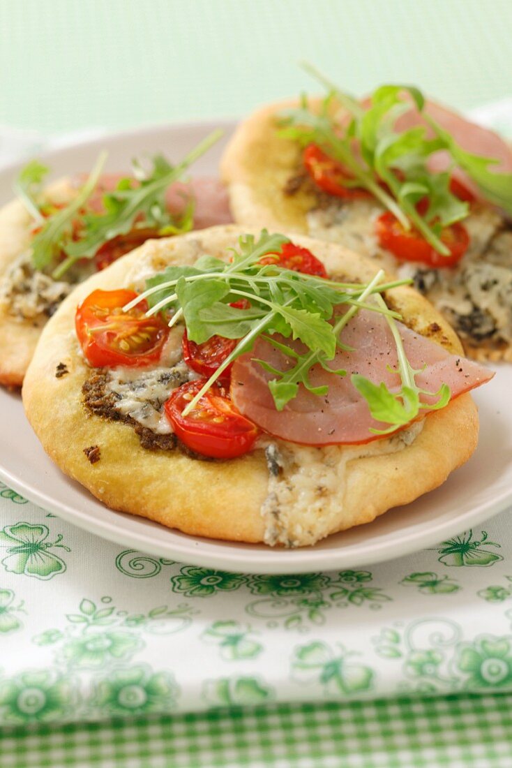 Mini pizzas with ham, blue cheese, rocket and cherry tomatoes