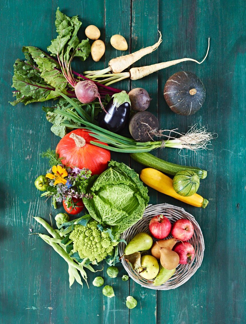 Various vegetables and a basket of stone fruits on a green wooden surface