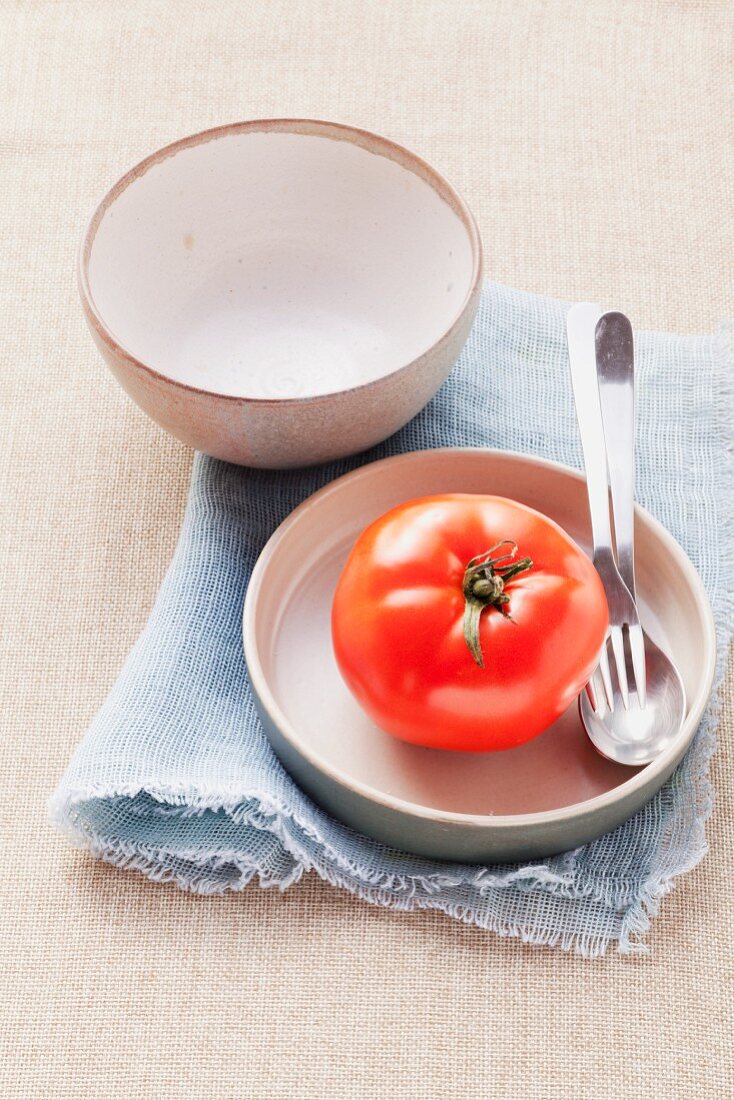 Eine Tomate auf einem Teller und eine leere Schale