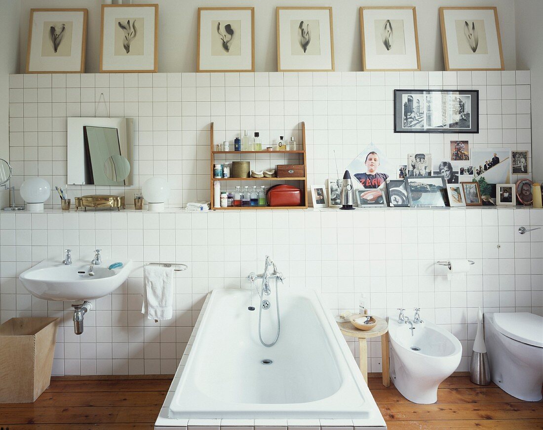 Bathroom fittings against white-tiled wall and framed pictures on shelf