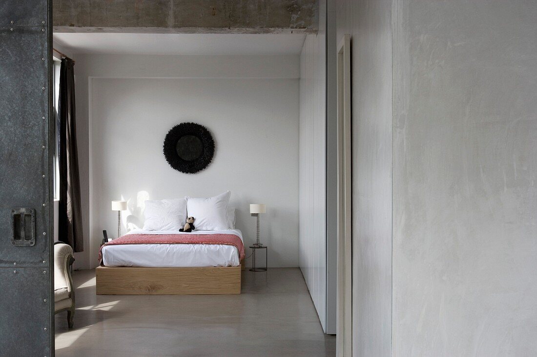 View of simple double bed in bedroom with screed floor through open door