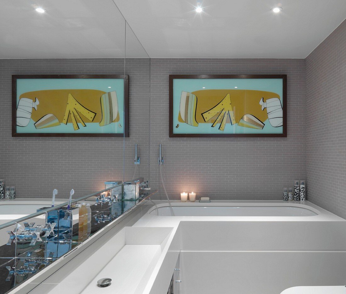 Washstand against mirrored wall and modern picture above bathtub in designer bathroom