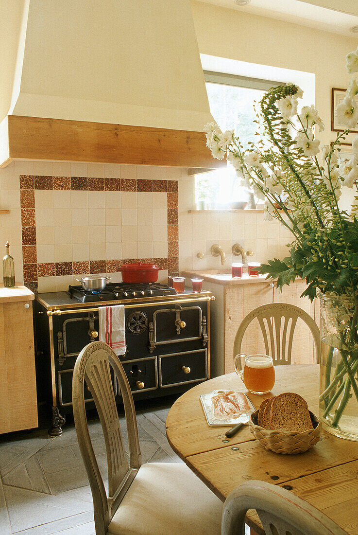 Country-style kitchen with wooden chairs and rustic oven, floral decorations on the table