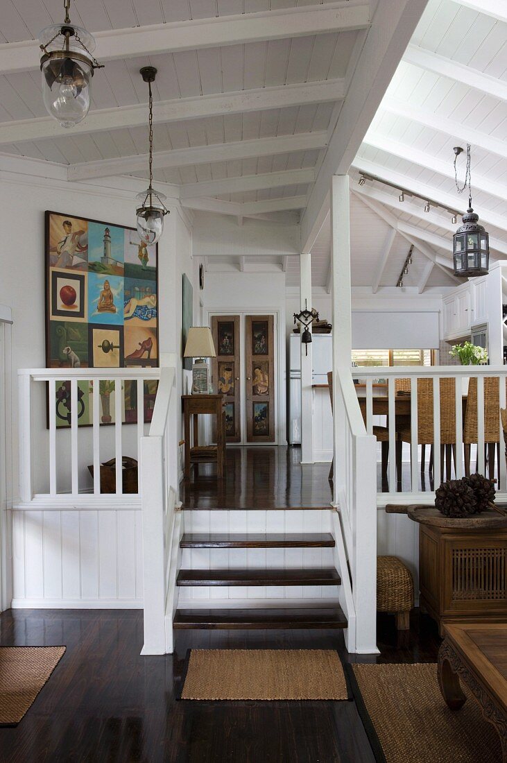 Open-plan interior with steps leading to gallery in rustic house with white wooden ceiling
