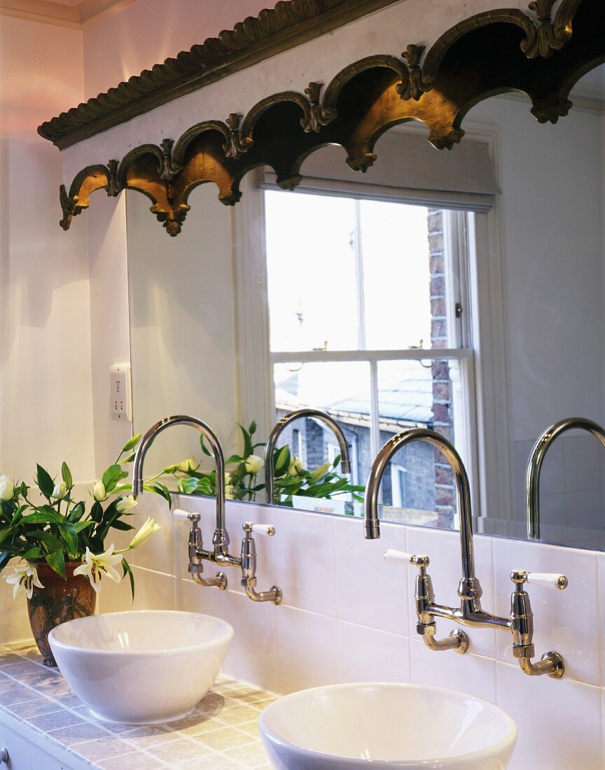 Wash basins on tiled washstand with vintage-style, wall-mounted tap fittings below mirror