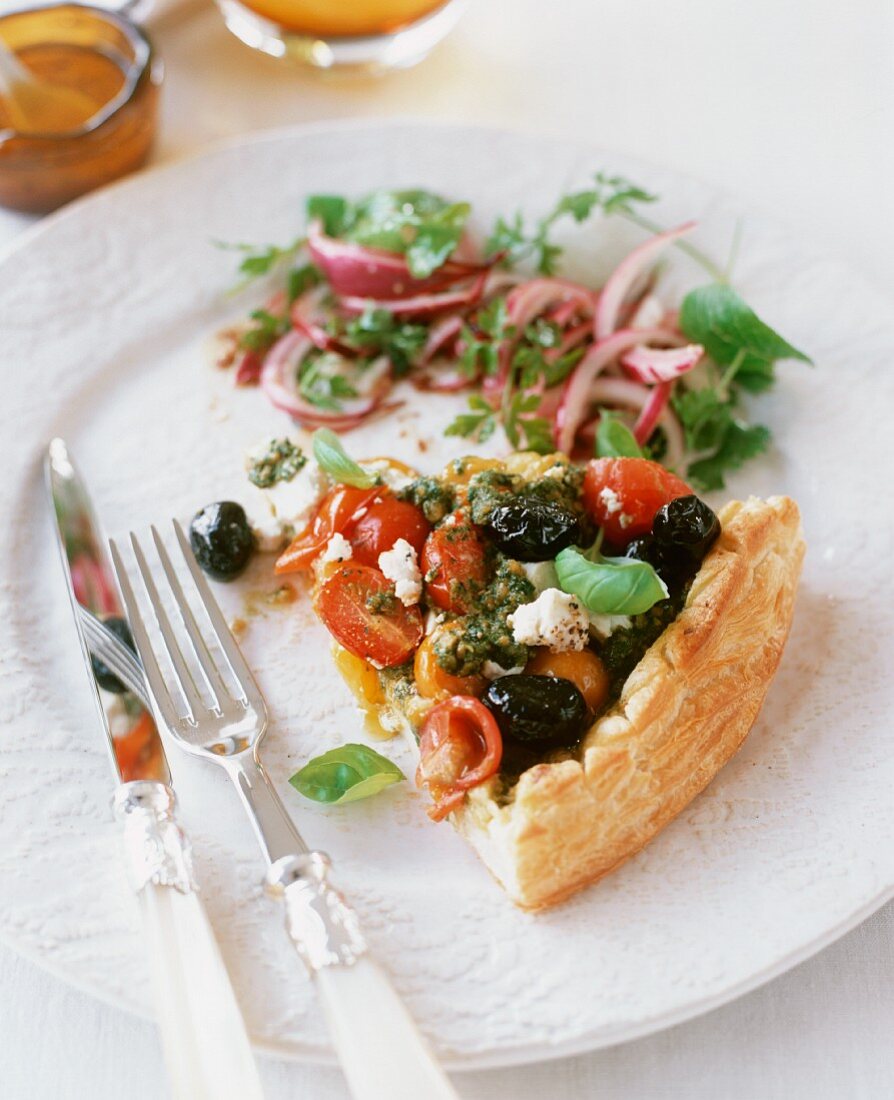 Ein Stück Tarte mit Ricotta, schwarzen Oliven, Kirschtomaten und Basilikum