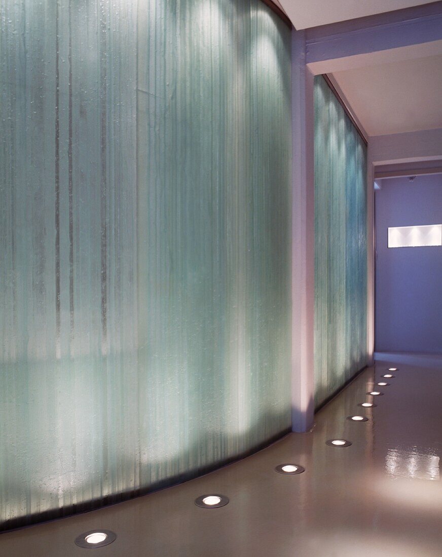 Polished screed floor with integrated floor lights in front of curved wall of exposed concrete