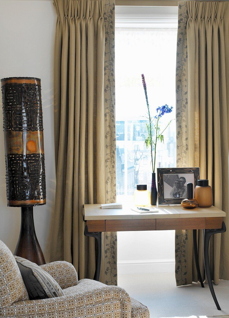 Small desk below window with traditional curtains and Africa-style standard lamp