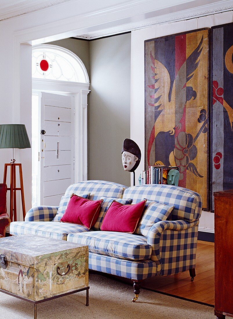 Living room with checked sofa, chest serving as coffee table & artworks on boards