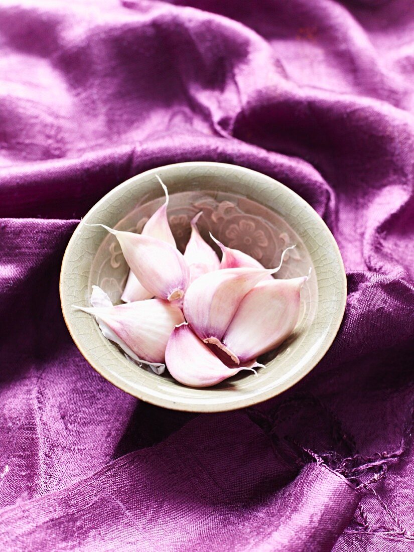 Cloves of garlic in bowl on purple cloth