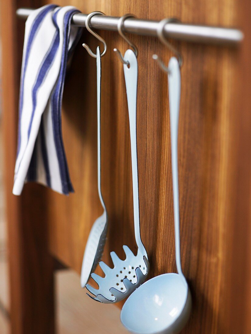 Vintage white enamelled kitchen utensils hanging on hooks on a wooden wall