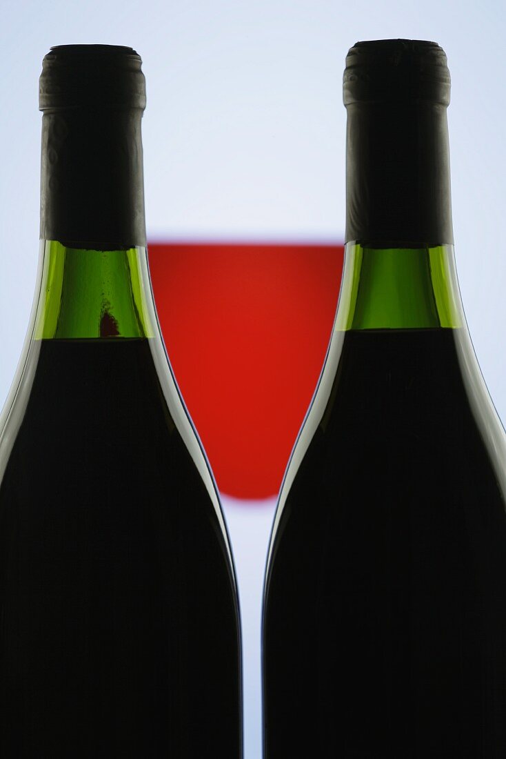 Zwei Flaschen Rotwein, dazwischen ein Rotweinglas