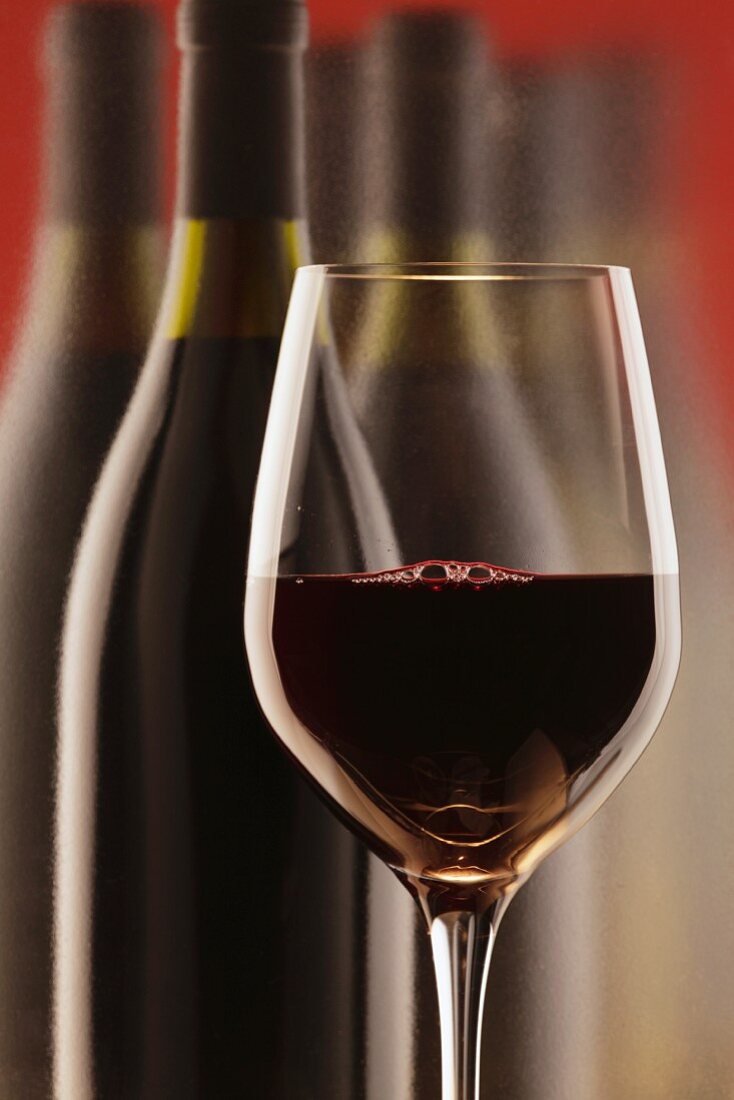 Ein Rotweinglas vor Rotweinflaschen