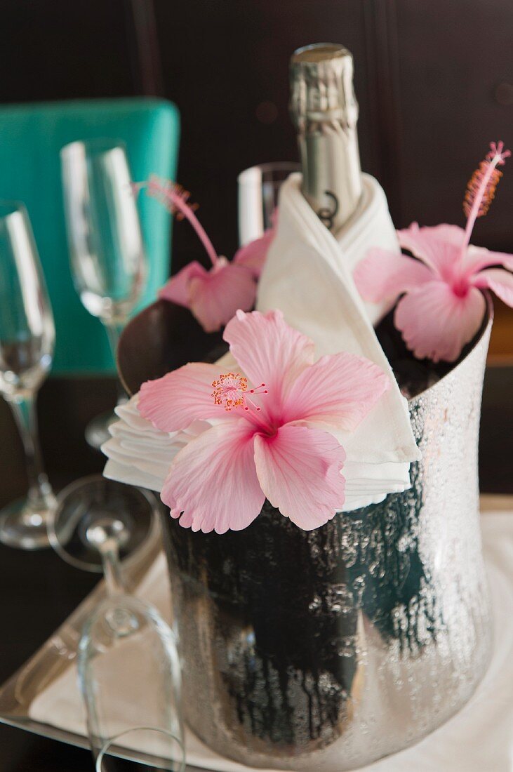 A bottle of champagne in a chiller decorated with hibiscus flowers